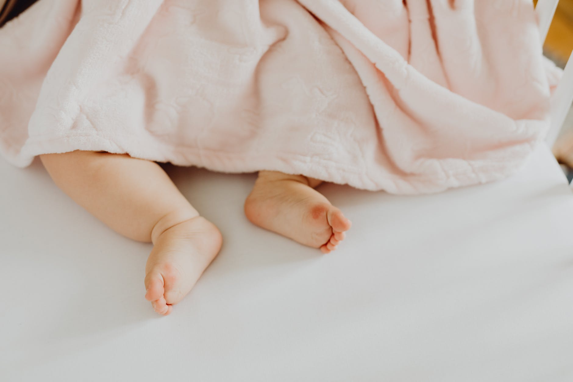 baby lying on white linen with pink blanket